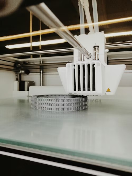 Industrial 3D printer extruder printing a circular precision part on a glass build plate — aerospace applications